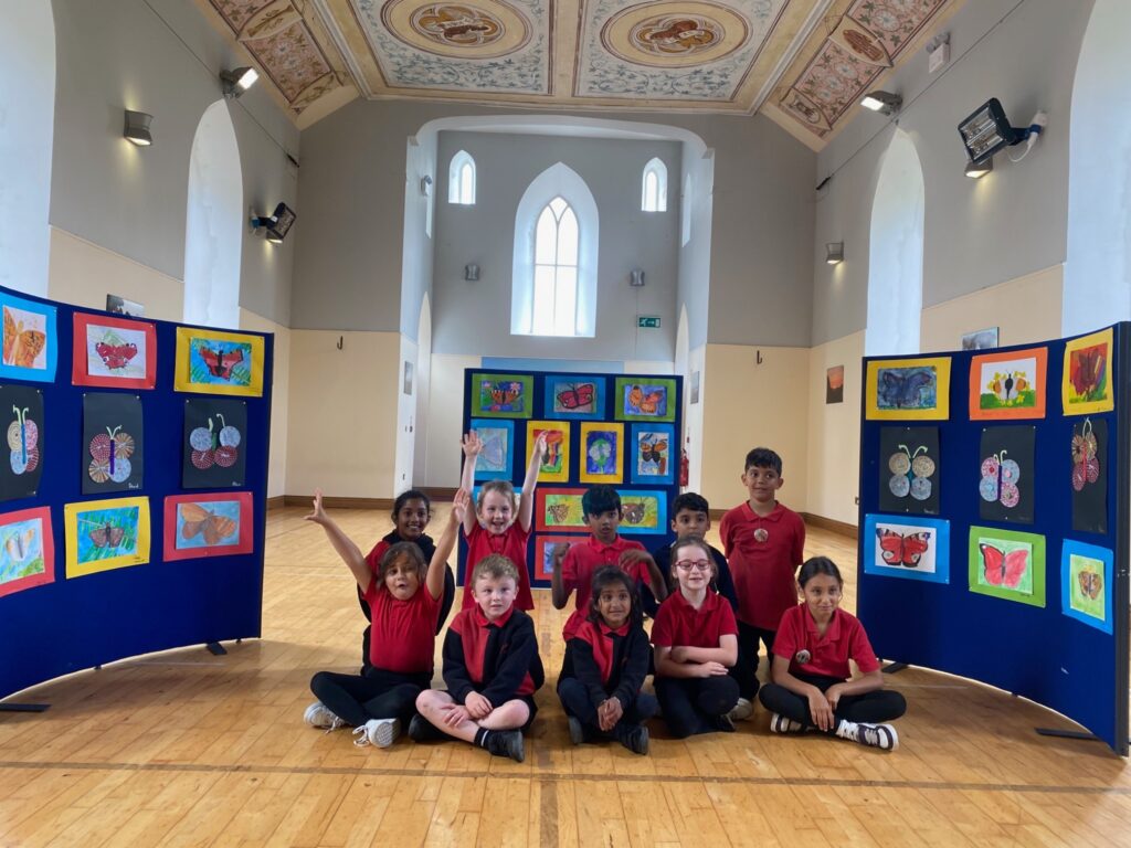 Happy junior, senior and 1st Class pupils showing their art butterflies