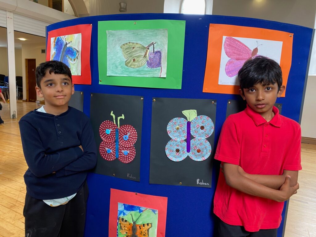 Happy junior, senior and 1st Class pupils showing their art butterflies