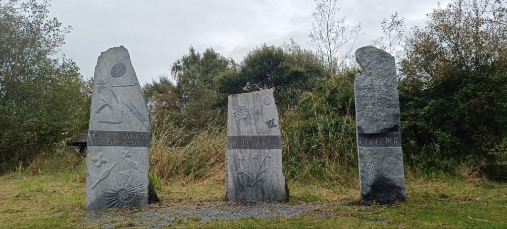 Photograph of three sculpted standing stones with the words ‘earth works because it all works together’ carved across the forward face of the stones