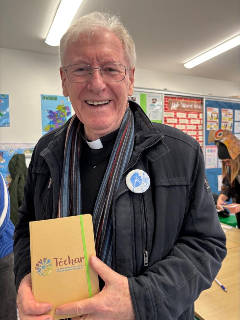 Photo of Fr Michael with a gift Tóchar notebook and a badge made from the children’s artwork (Photo Helen Shaw