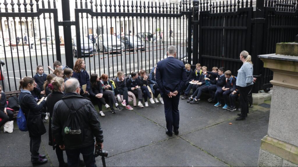 Photograph of the St Anne's National School children seated having a briefing in the shadow of Dáil Eireann with Minister O’Sullivan answers questions from the class (Stephen Crilly - Tóchar Stories). 