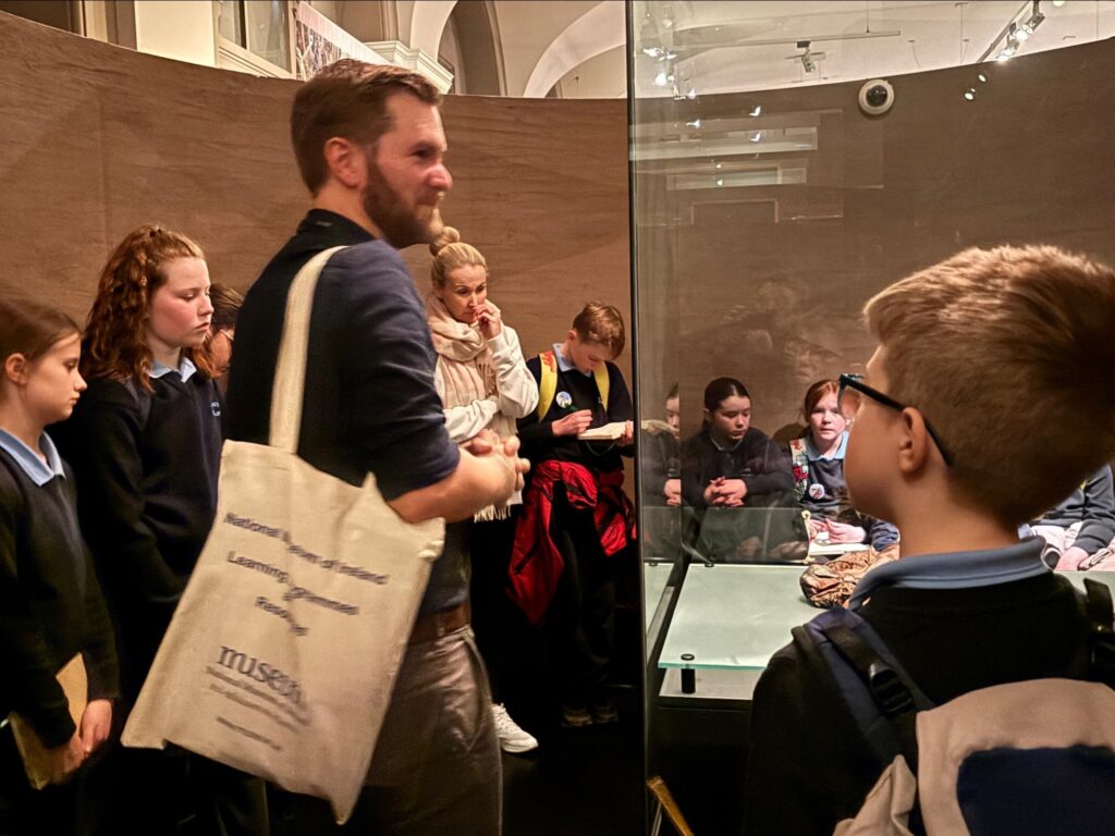 Photograph of National Museum Guide, Matthew Lester in the exhibit of the bog bodies, with Amber and her classmates around him. (Helen Shaw - Tóchar Stories).