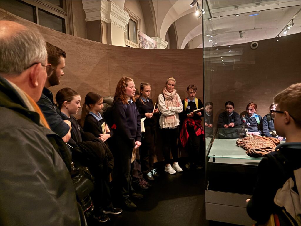 Photograph of school child, Amber telling the story of Croghan man as both Matthew, Eugene, Dawn (the class assistant) and her classmates listen on (Helen Shaw - Tóchar Stories). 