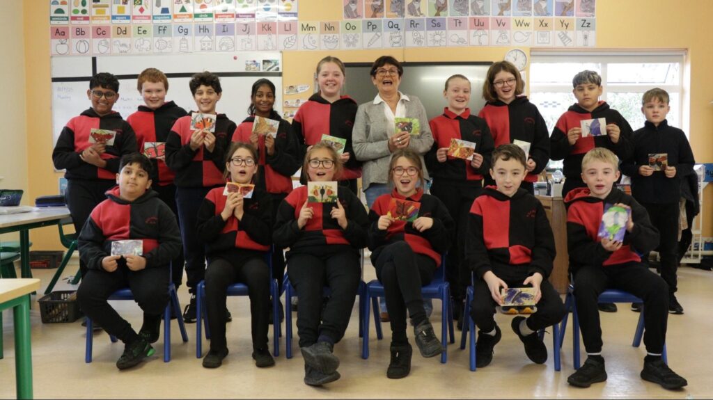 Photograph of Eileen Fahey from Kilteevan Tidy Towns, with the children from Kilteevan NS senior class and the postcards of their bog butterfly artwork