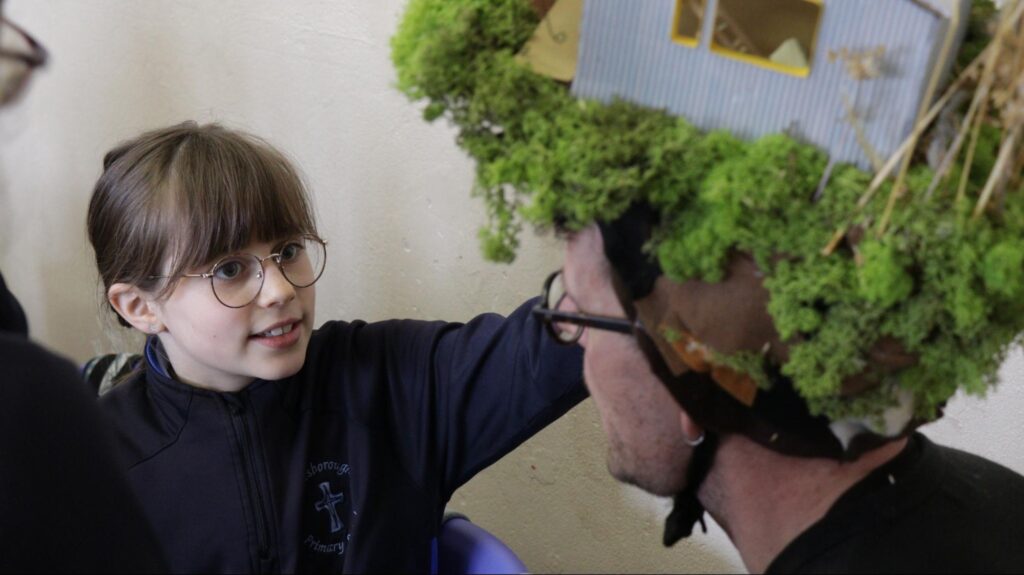 Photograph of pupil in Lanesborough Primary School admiring artist Luke Casserly’s ‘bog bothy’ hat during a Tóchar Stories creative bog nature workshop in the school ( credit Stephen Crilly)