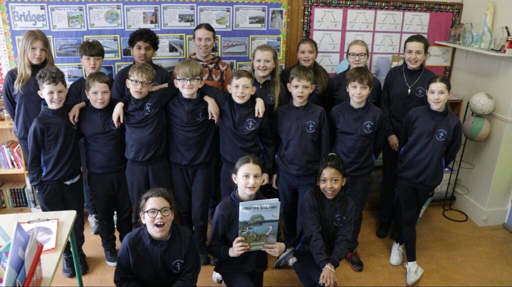 Photograph of Adam Mulvihill, Longford Biodiversity Officer, with the 5th and 6th Classes, Lanesborough Primary School with one of the pupils holding up the Longford Boglands Wildlife Workbook in the front row (credit Stephen Crilly)