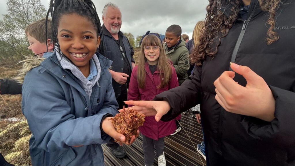 Photograph of the children getting to feel sphagnum moss with Noel Carberry, OPW guide in the background (credit Helen Shaw)