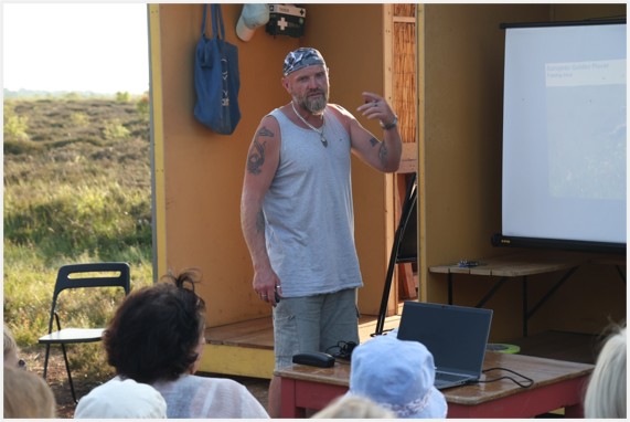 Man stands facing a crowd, with a presentation screen behind him.