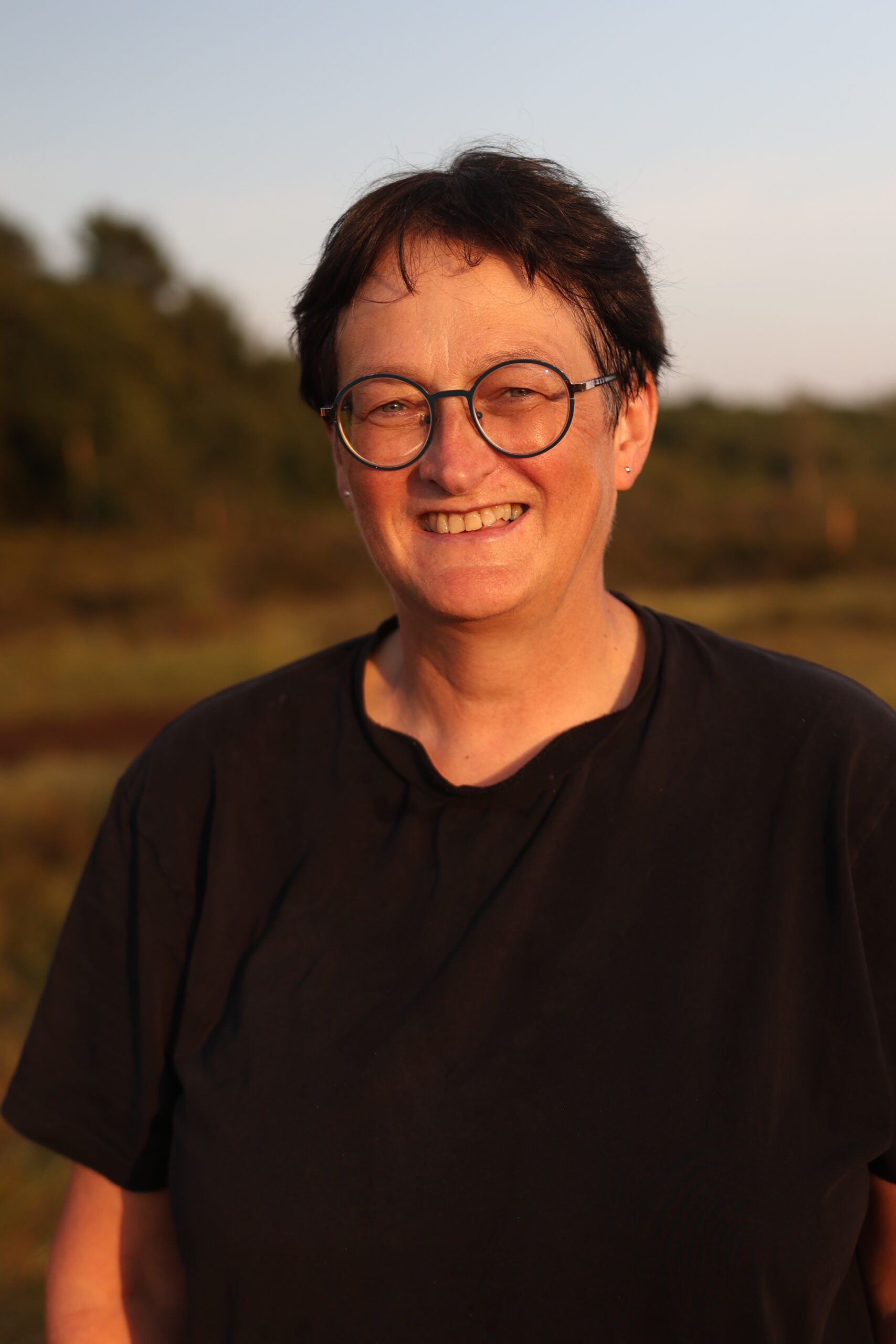 Woman, wearing round glasses, smiling. 