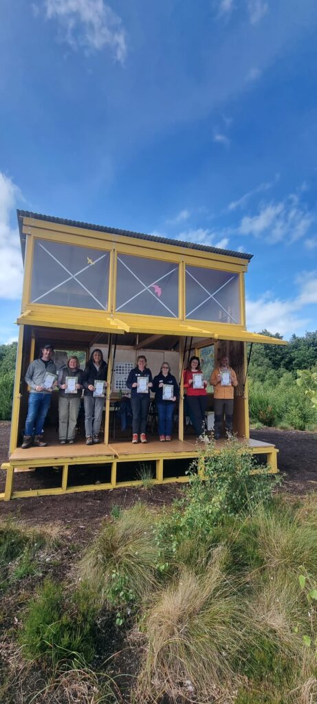 Group of people standing in bog bothy holding certifications for leave no trace awareness course