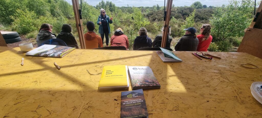 Photo taken inside bog bothy with group of standing with backs to the camera and listening to instructor