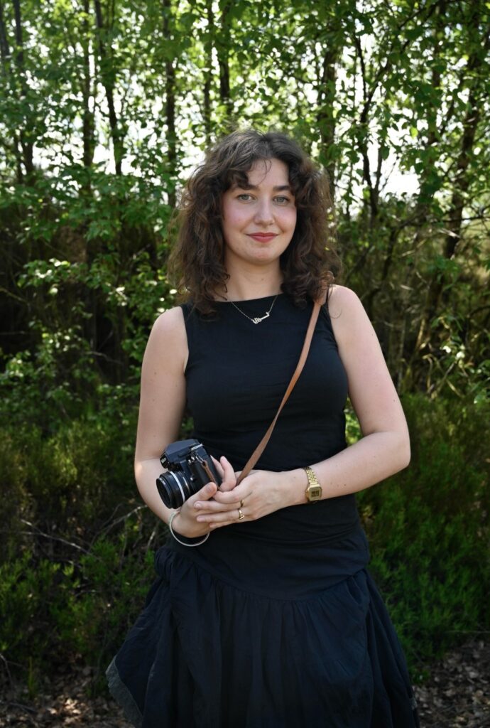 Evanna Devine holding her camera standing in front of greenery