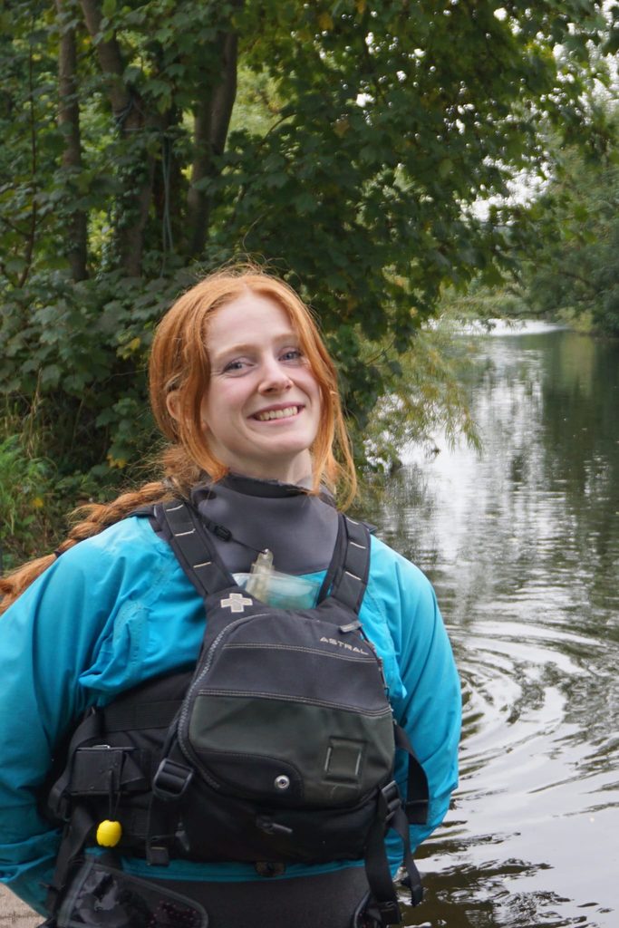 Woman standing in wet gear and life jacket smiling by a river