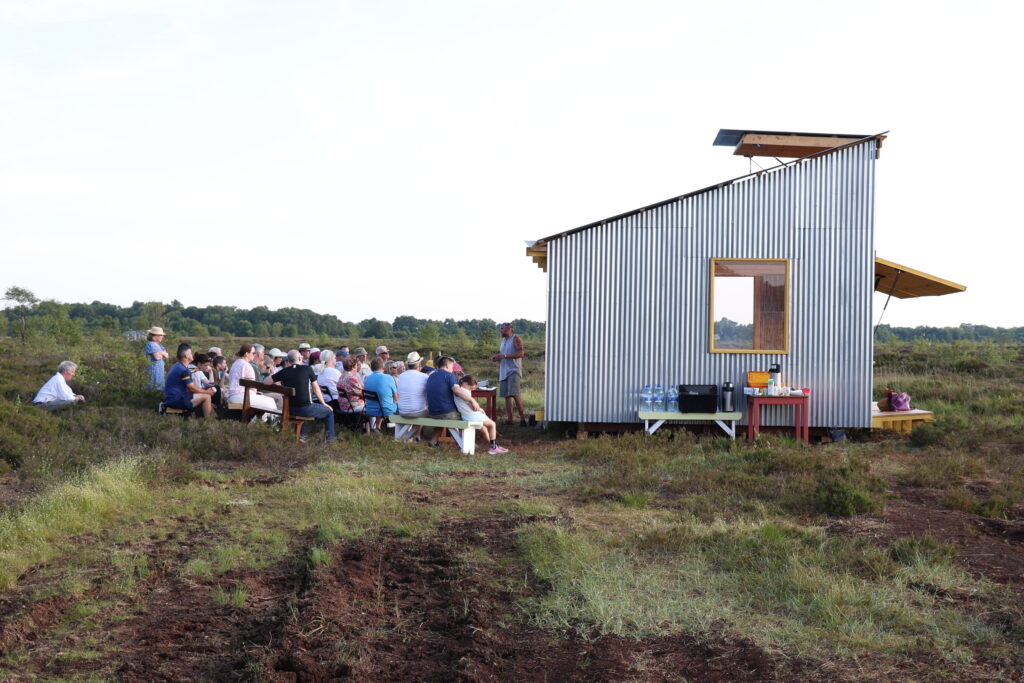 Crowd sitting outside bog bothy listening to speaker