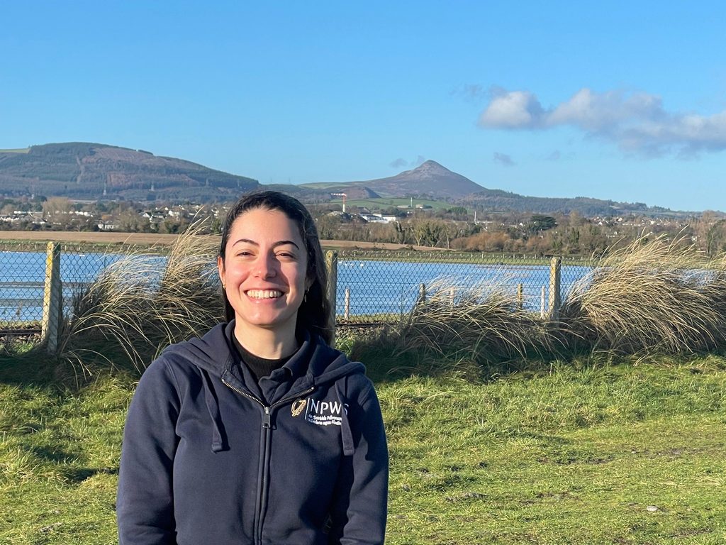 Woman standing outside smiling with mountains and a river in the background