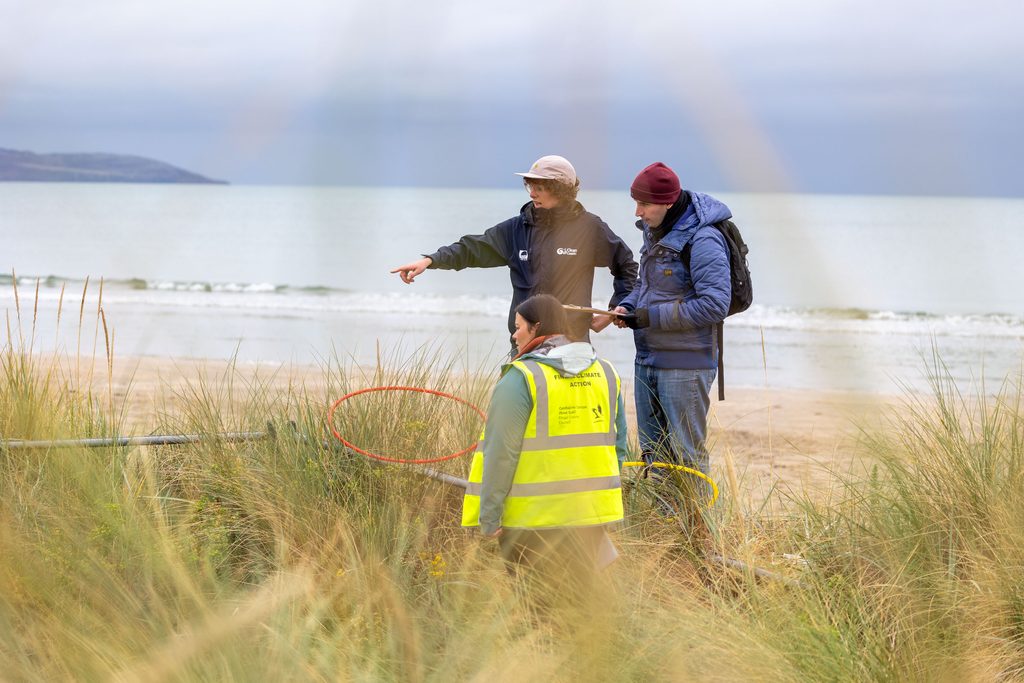 Three people standing on a dune on a beach