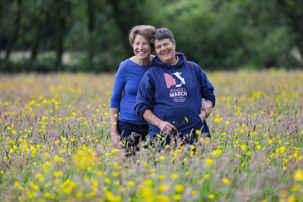 Two women standing in a meadow smiling and looking at the camera.