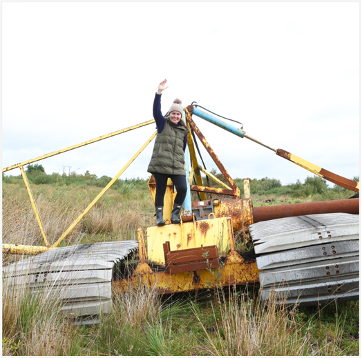 Woman standing and waving from on top of abandoned Bord na Móna machinery on Cloontuskert bog.